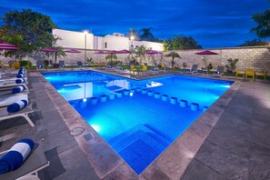 A swimming pool with lounge chairs and umbrellas, surrounded by a stone wall and trees.