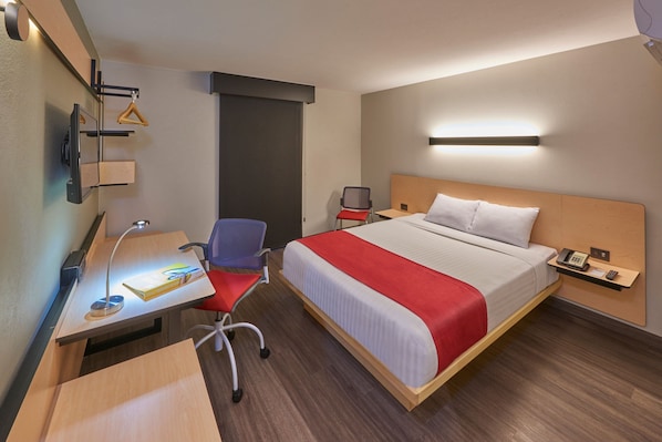 Une chambre d’hôtel comprenant un lit, un bureau, une chaise et une petite table avec une lampe.