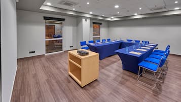 Uma sala de conferências com uma mesa comprida, cadeiras azuis e um armário de madeira.