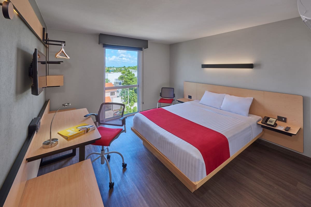 Une chambre d’hôtel équipée d’un lit, d’un bureau, d’une chaise et d’une fenêtre donnant sur des immeubles.