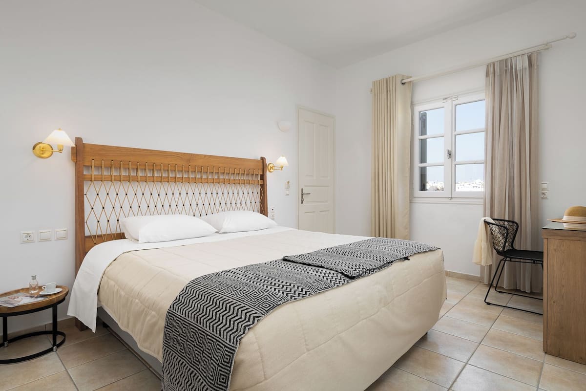 A neatly arranged hotel room with a large bed, a bedside table with a lamp, a chair, and a window with curtains.