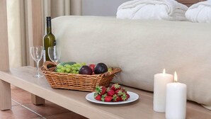 A bedroom with a bed, a bedside table with a basket of fruits, two candles, and a wine bottle. - Astir of Naxos (Naxos)
