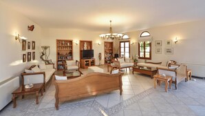 A spacious living room with a large wooden sofa, multiple armchairs, a television, and a chandelier. - Astir of Naxos (Naxos)