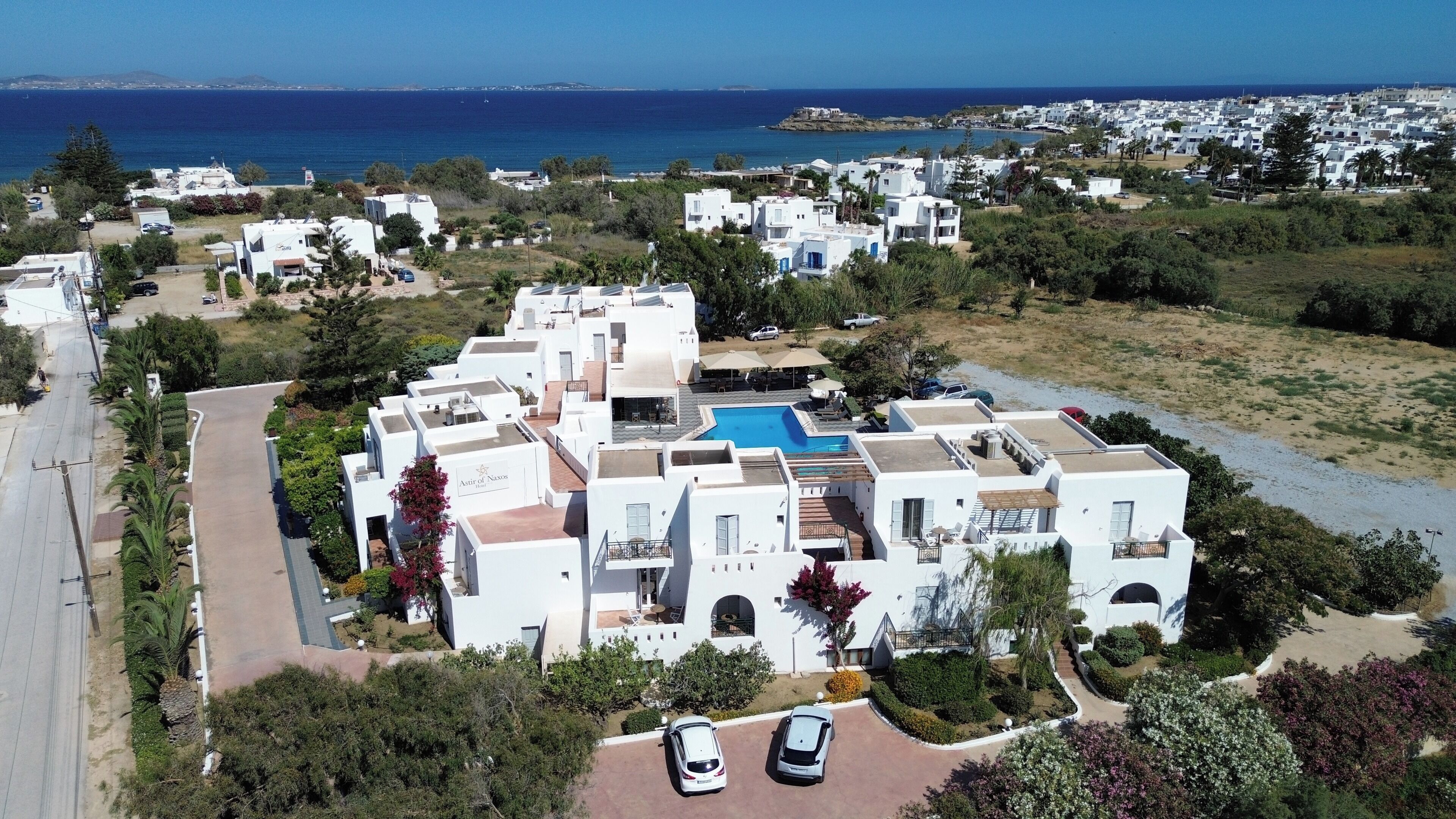 A residential area with white buildings, a swimming pool, and a view of the sea.