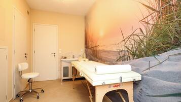 A room with a massage table, a chair, a sink, and a wall mural.