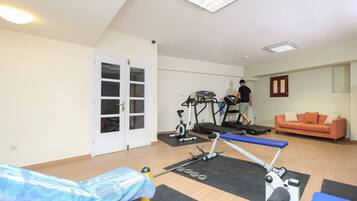 Un gimnasio con equipamiento de ejercicio, cinta de correr, banco y camilla de masaje.