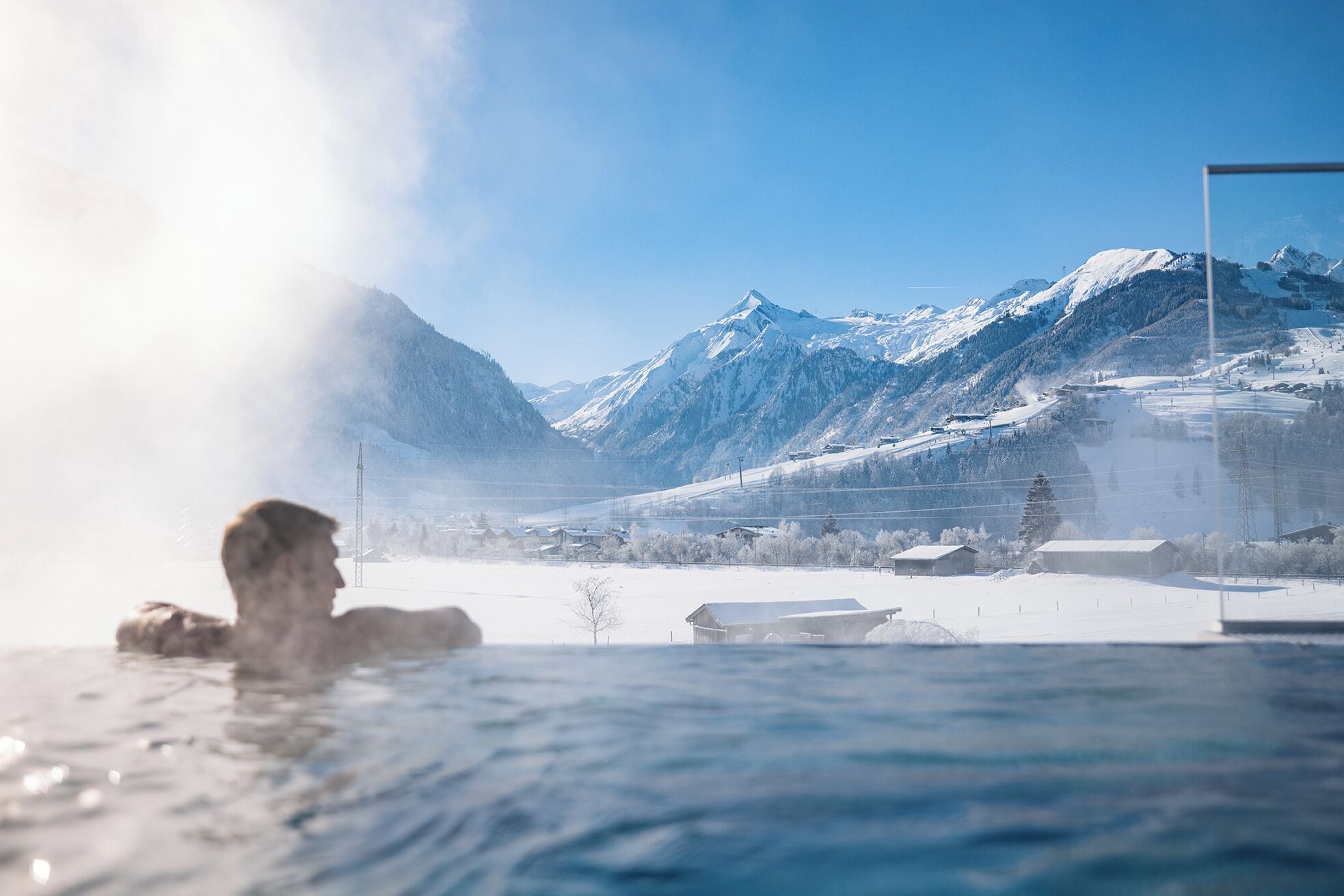 Une personne dans un bain à remous, avec vue sur un paysage montagneux enneigé.