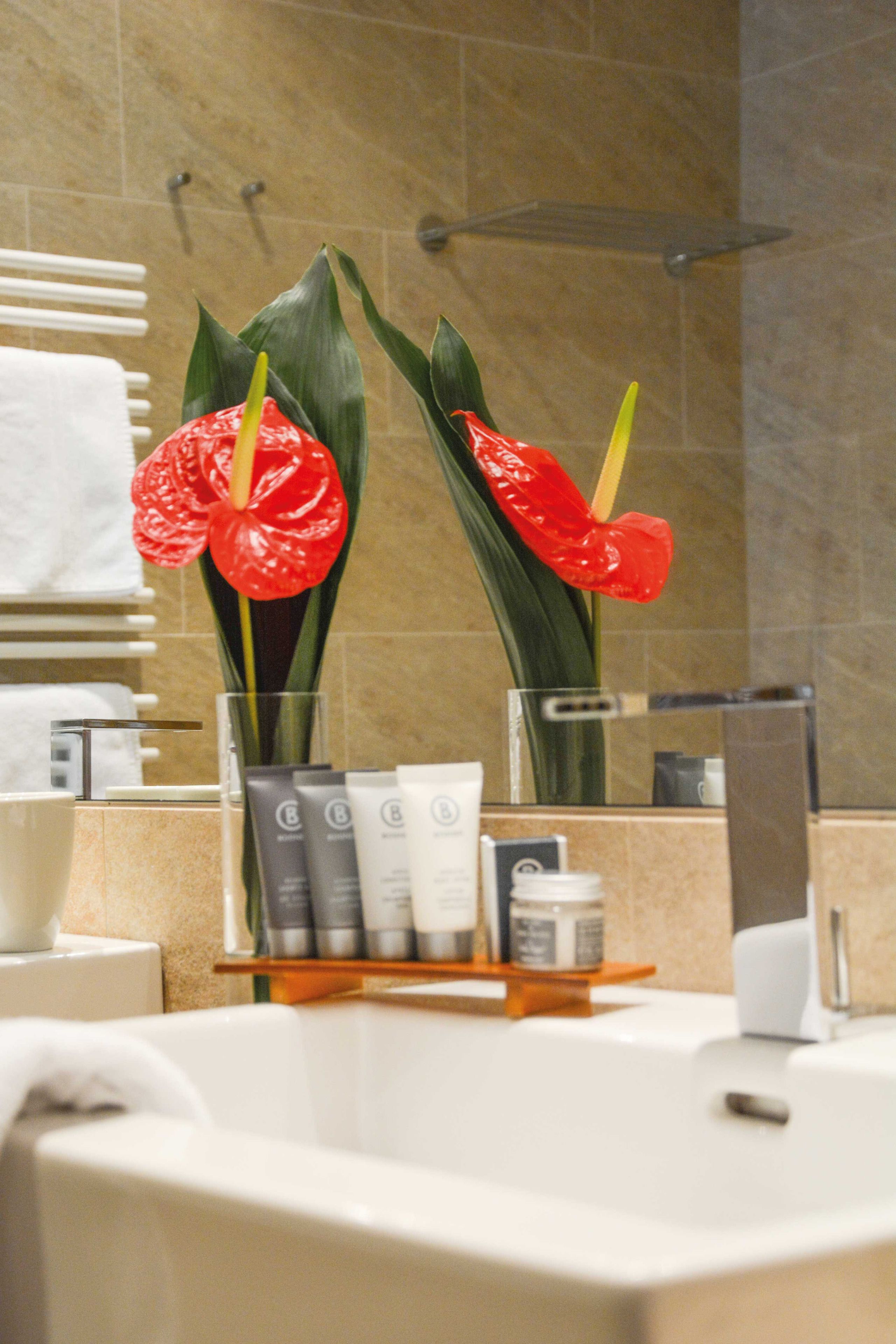 A bathroom with a bathtub, toiletries, and two red flowers.