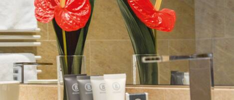 A bathroom with a bathtub, toiletries, and two red flowers.