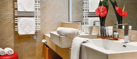 Un baño moderno con dos lavamanos, toallas blancas, un taburete rojo y un espejo con flores rojas.