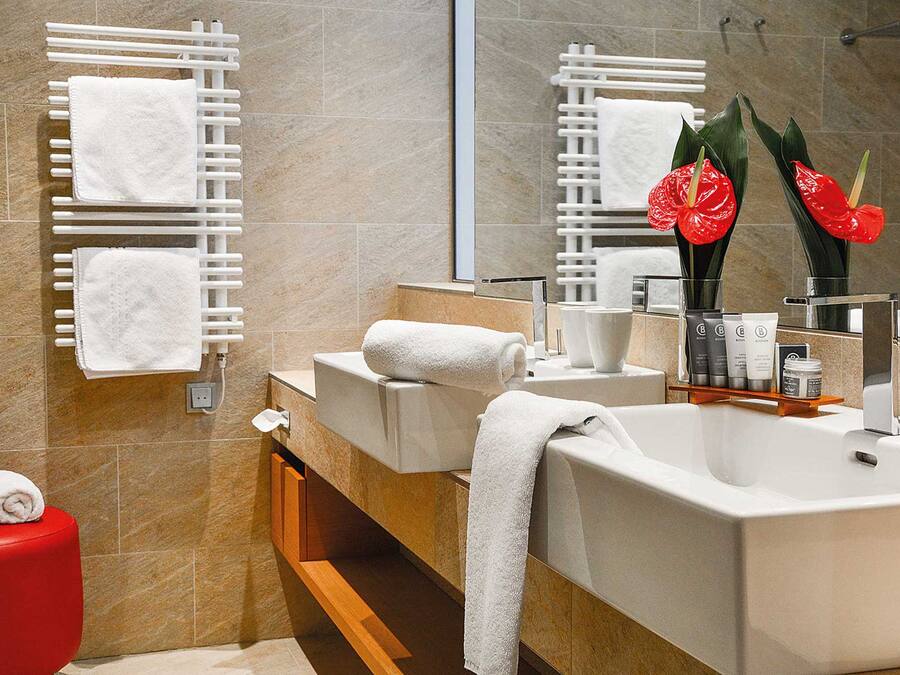Une salle de bain moderne avec deux lavabos, des serviettes blanches, un tabouret rouge et un miroir décoré de fleurs rouges.