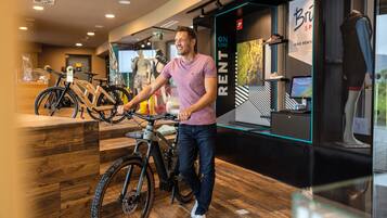 En mand står ved siden af en cykel i et moderne, indendørs rum med trægulv og glasvægge.