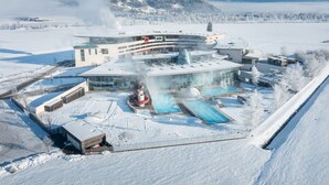 A modern building with a curved roof, surrounded by snow-covered fields and mountains. - TAUERN SPA Zell am See - Kaprun (Kaprun)