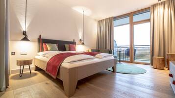 A modern hotel room with a large bed, two bedside tables, a balcony with a view, and a wooden floor.