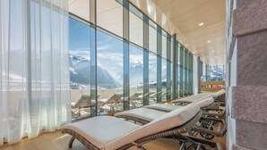 A modern indoor area with large windows overlooking a snowy mountain landscape. There are several reclining chairs with cushions. - TAUERN SPA Zell am See - Kaprun (Kaprun)