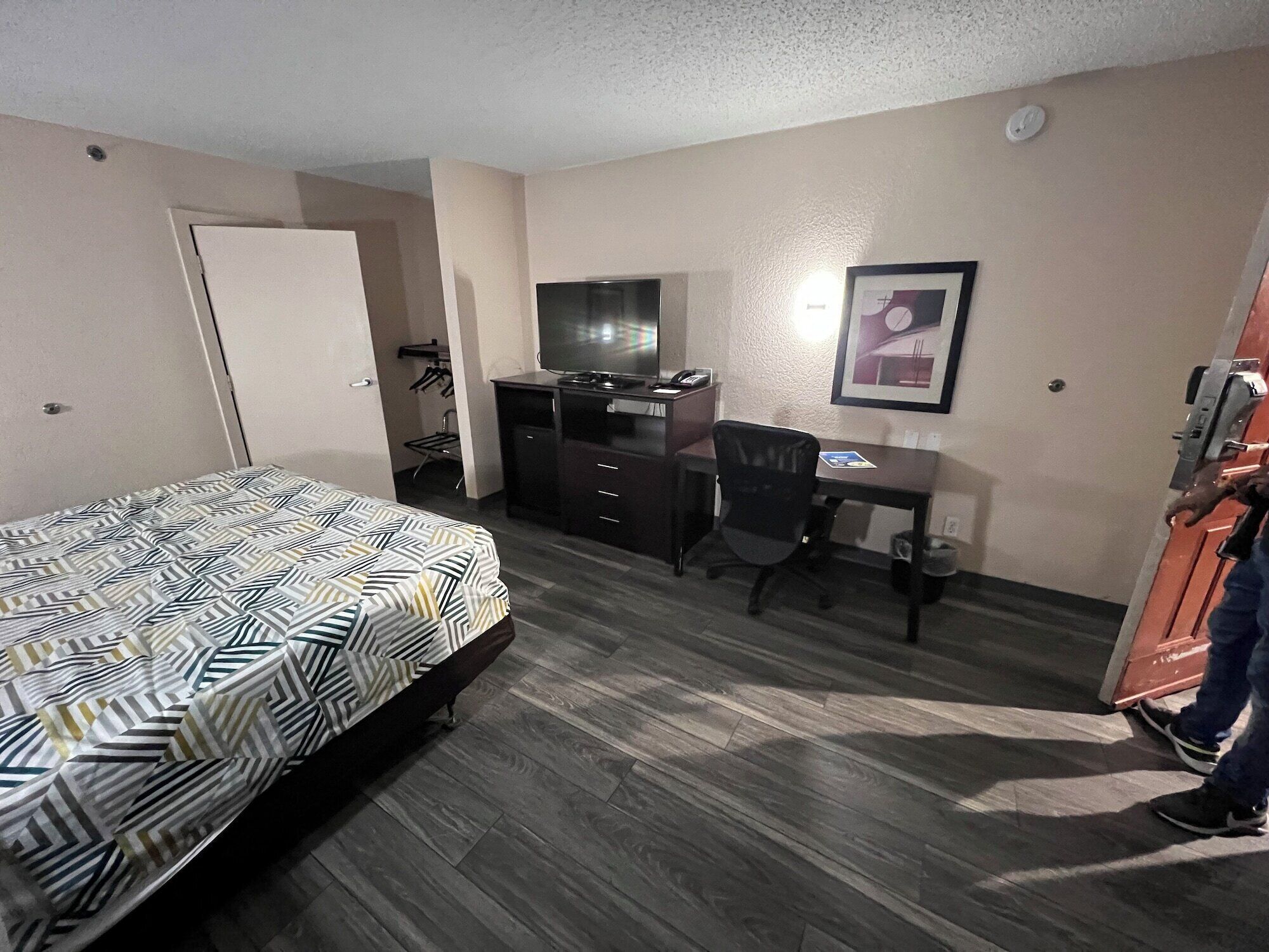 A hotel room with a bed, a desk, a chair, a television, and a framed picture on the wall.