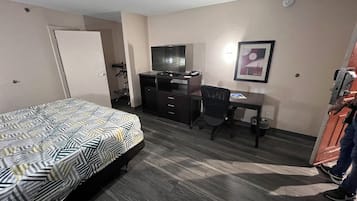 A hotel room with a bed, a desk, a chair, a television, and a framed picture on the wall.