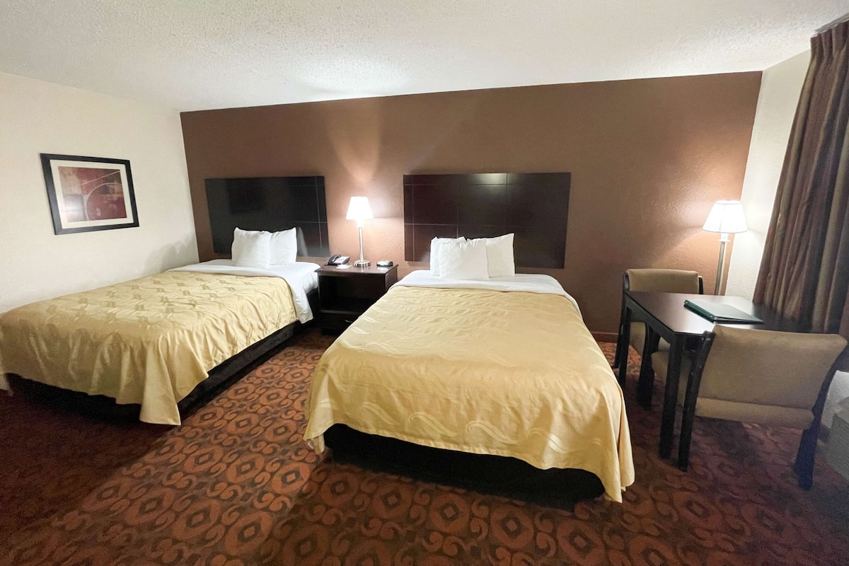 Une chambre d’hôtel avec deux lits, un bureau, une chaise et une table de chevet avec une lampe.