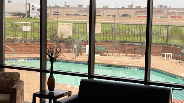 A view of a swimming pool with a fenced area, a bench, and a table with a vase. - Motel 6 Oklahoma City, OK - Fairgrounds West (Oklahoma City)