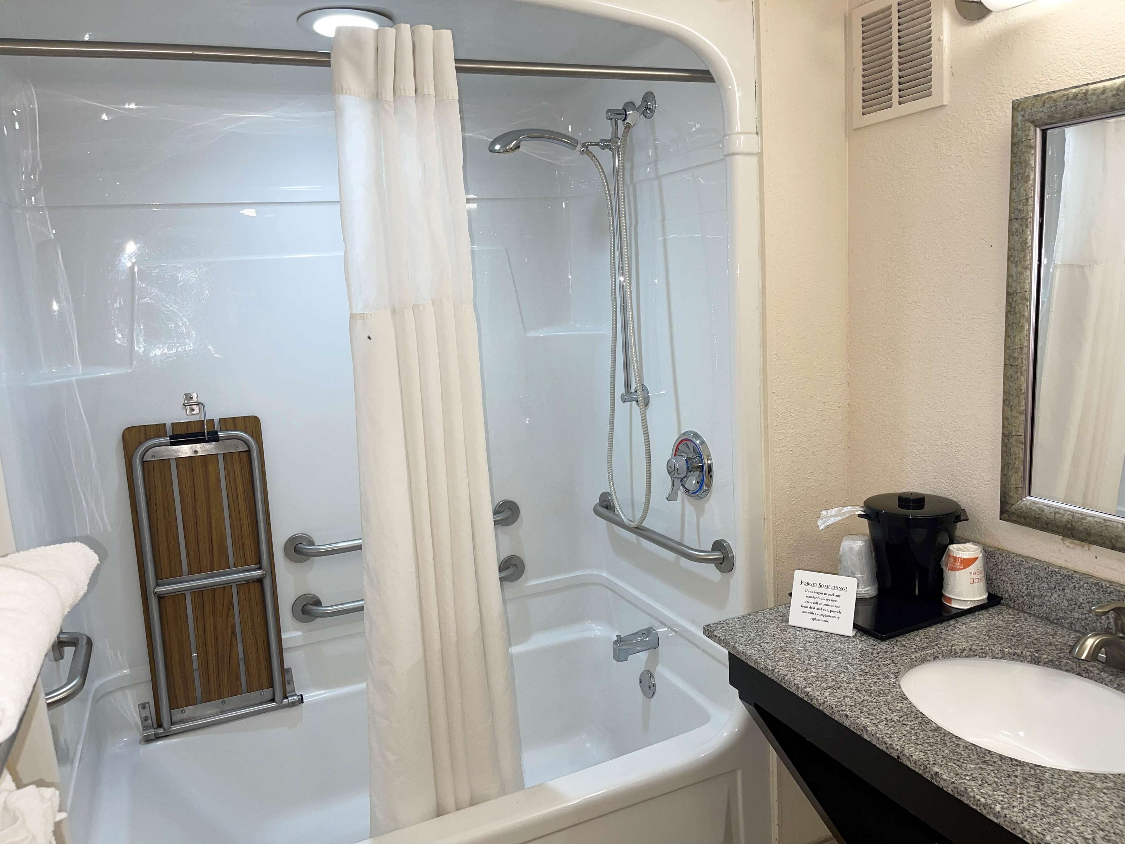 A bathroom with a shower, a grab bar, a sink, and a mirror.