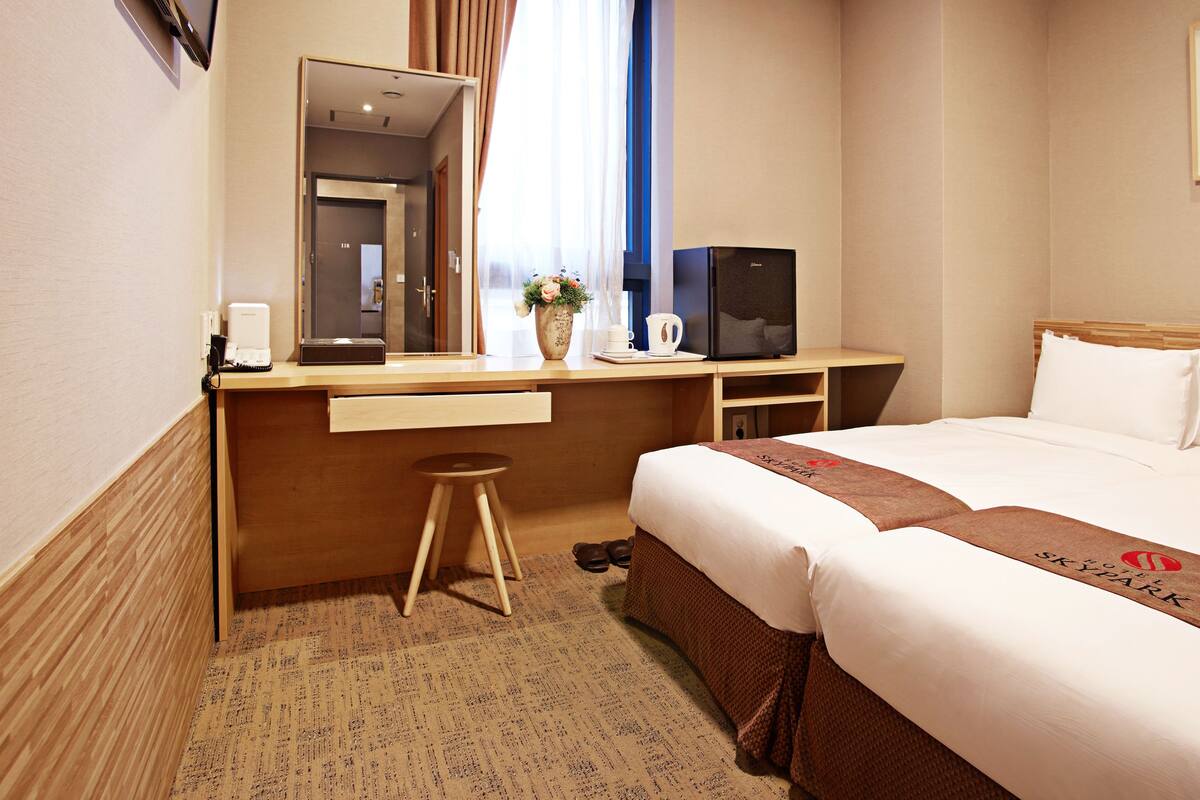 A hotel room with a bed, a desk with a computer, a chair, a mirror, and a window with curtains.