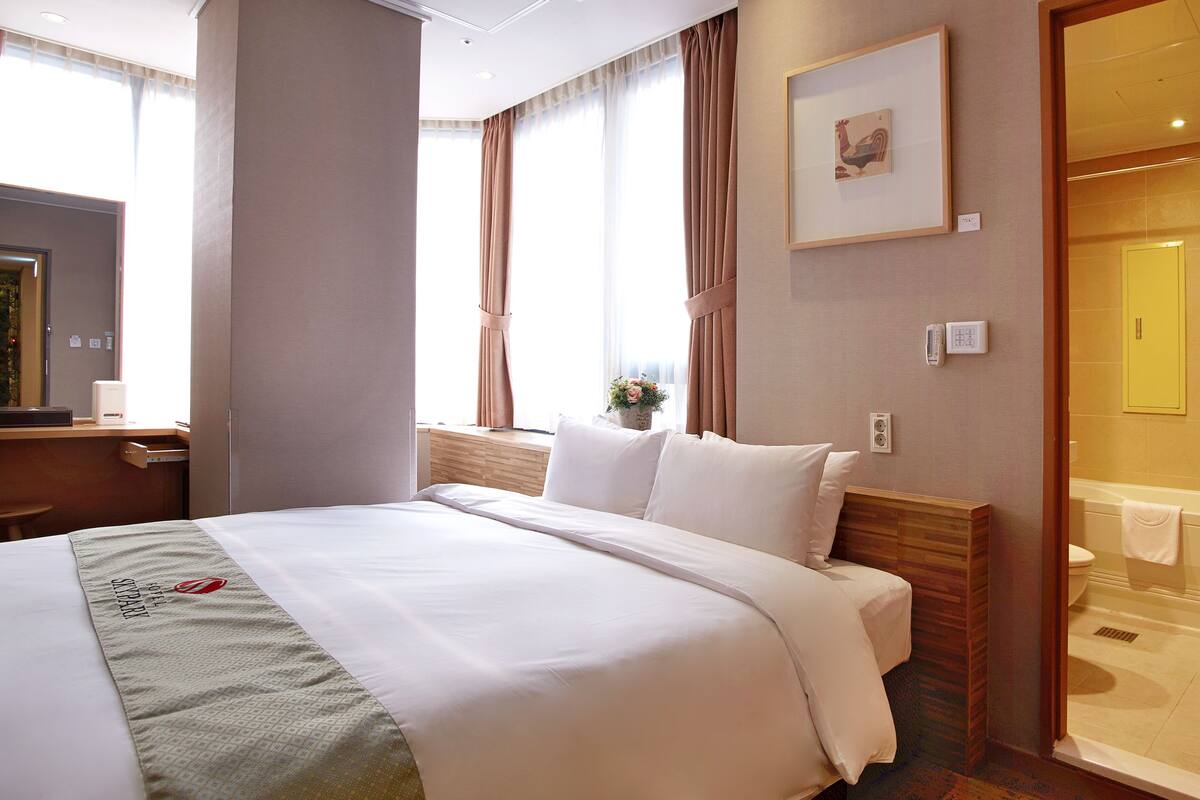 A hotel room with a bed, a desk, a phone, and a bathroom visible through an open door.