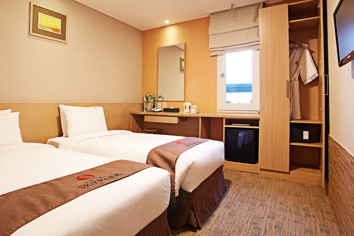 A hotel room with two beds, a desk, a mirror, a television, and a wardrobe.