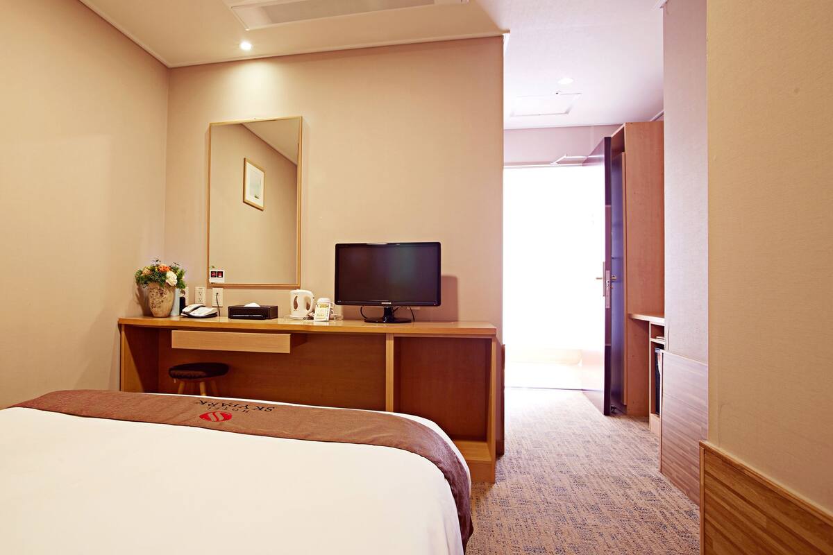 A hotel room with a bed, a desk with a computer, a mirror, and a door leading to another room.