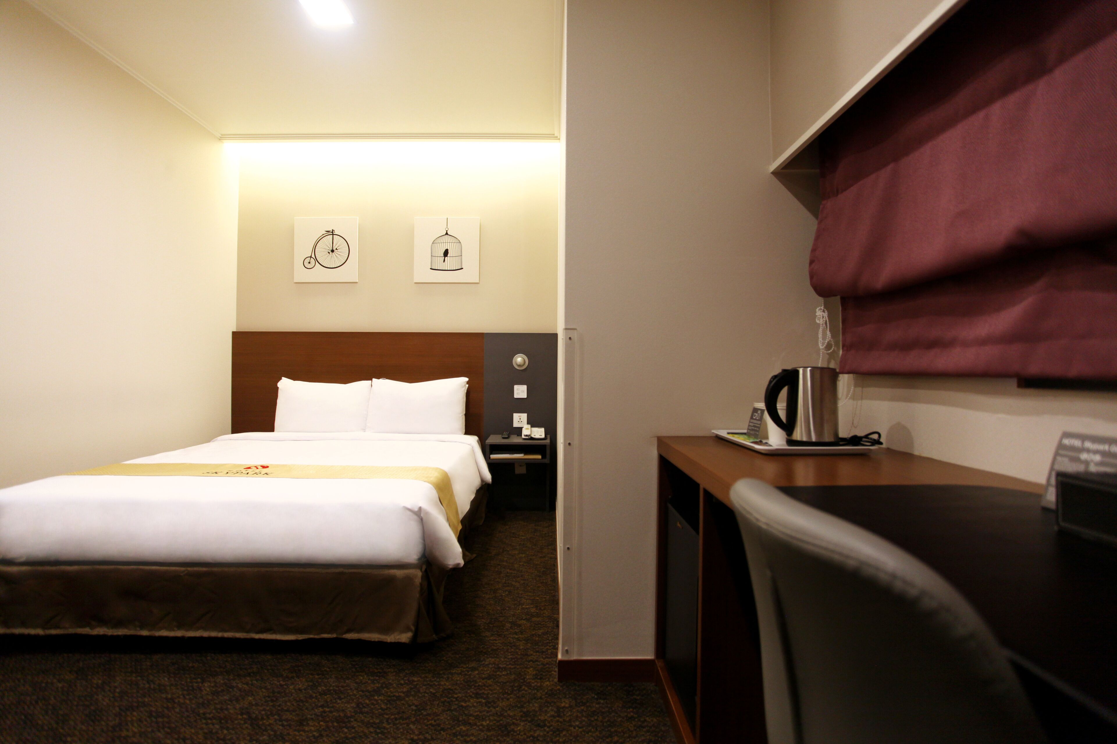 A hotel room with a bed, bedside table, lamp, and a desk with a chair.