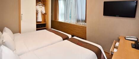 Habitación de hotel con dos camas, televisión, escritorio con teléfono y ventana con cortinas.