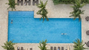 An aerial view of a rectangular swimming pool surrounded by palm trees and lounge chairs. - Joya Lofts and Towers (Makati)