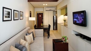 A modern living room with a sofa, a dining table, and a TV mounted on the wall. - Joya Lofts and Towers (Makati)