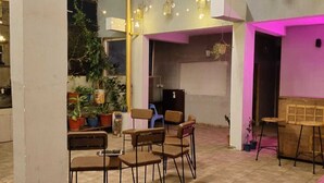 An outdoor patio area with tiled flooring, several chairs, a wooden table, and string lights. - Hotel Raghuraj Palace (Jaipur)