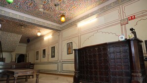 A room with a patterned ceiling, a wooden desk, and a bench. - Hotel Raghuraj Palace (Jaipur)
