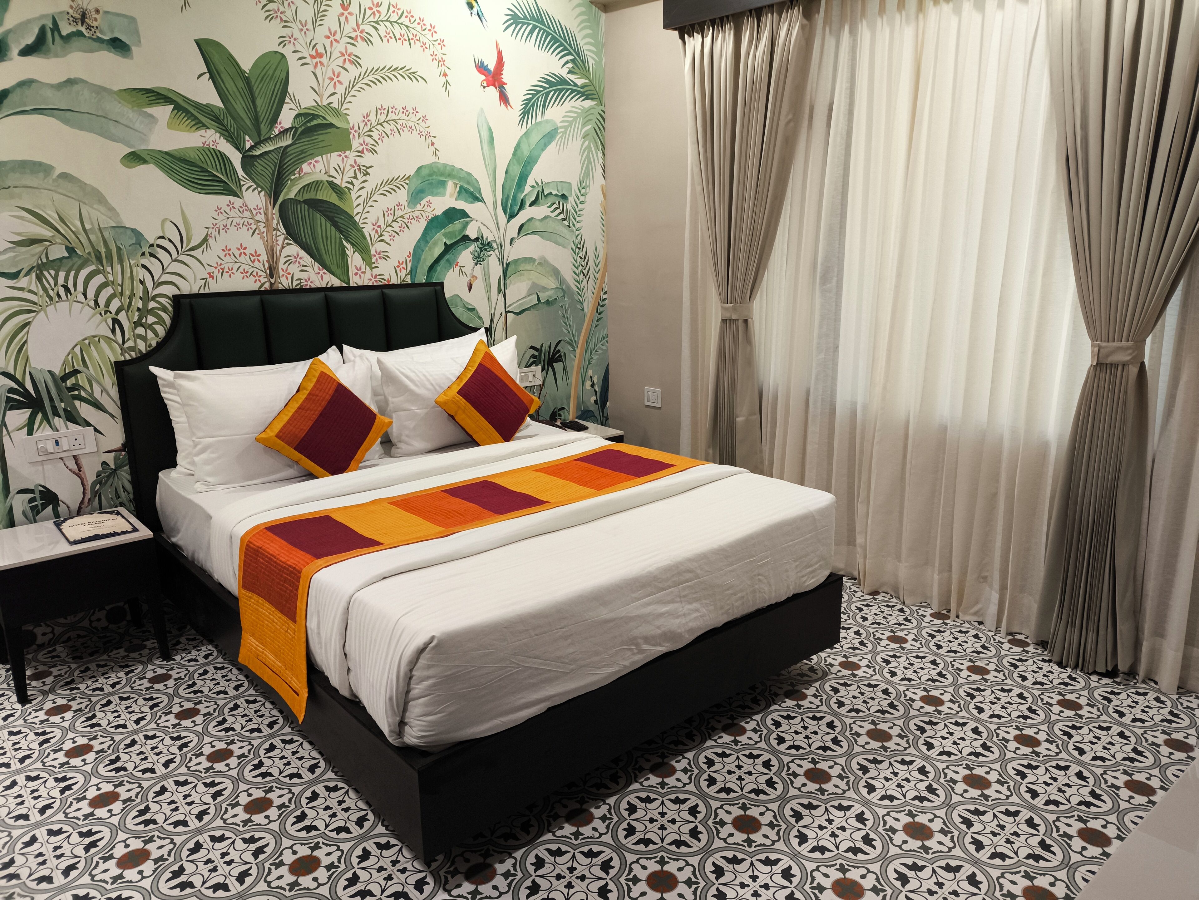 A neatly made bed with a patterned bedspread, a nightstand with a phone, and a wall with a tropical mural.