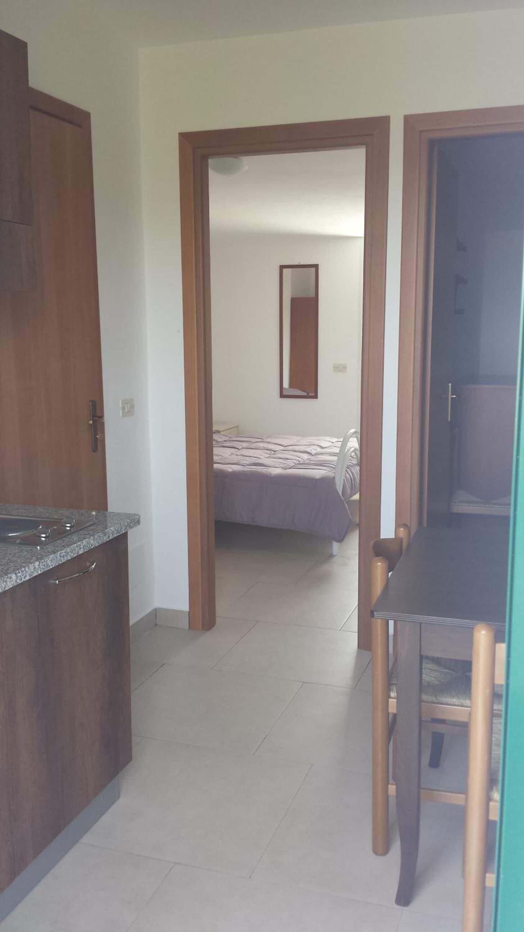 A compact hotel room with a kitchenette, a bed, and a mirror.