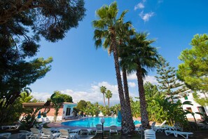 A pool area with lounge chairs, palm trees, and a clear blue sky. - Villaggio Alkantara (Giardini Naxos)