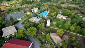 An aerial view of a residential area with a swimming pool, tennis court, and various buildings. - Villaggio Alkantara (Giardini Naxos)