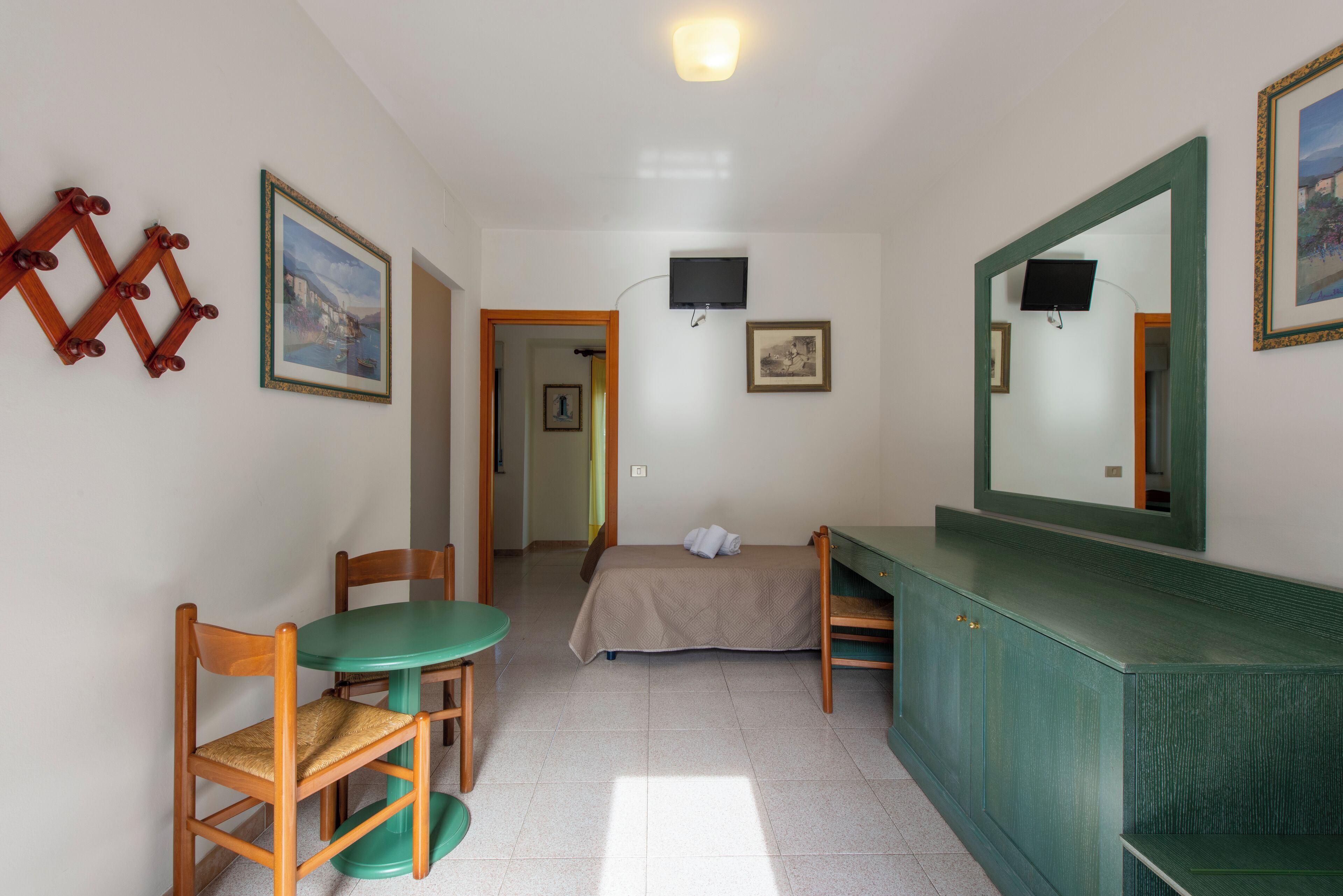Une petite pièce propre, avec un lit, un bureau, une chaise, une télévision et un miroir.