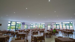 A spacious dining area with multiple tables and chairs, large windows, and a television screen on the wall. - Villaggio Alkantara (Giardini Naxos)