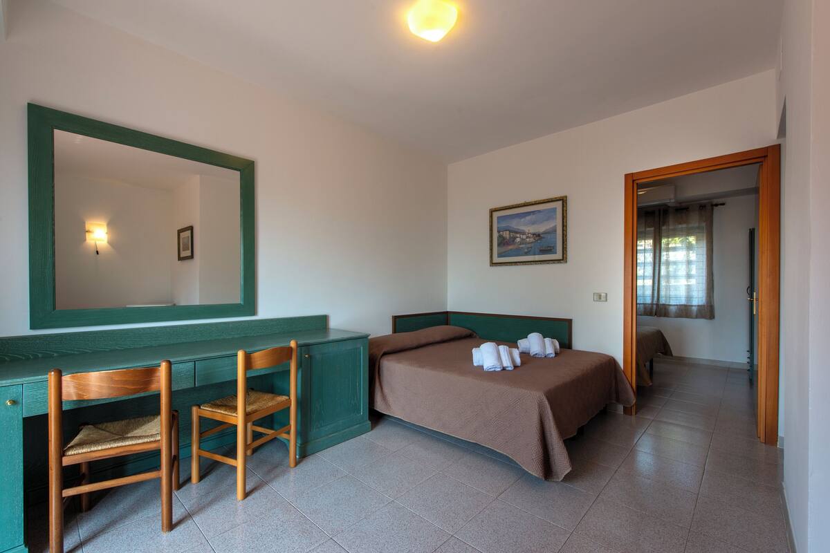 A bedroom with a bed, a desk with a chair, a mirror, and a painting on the wall.