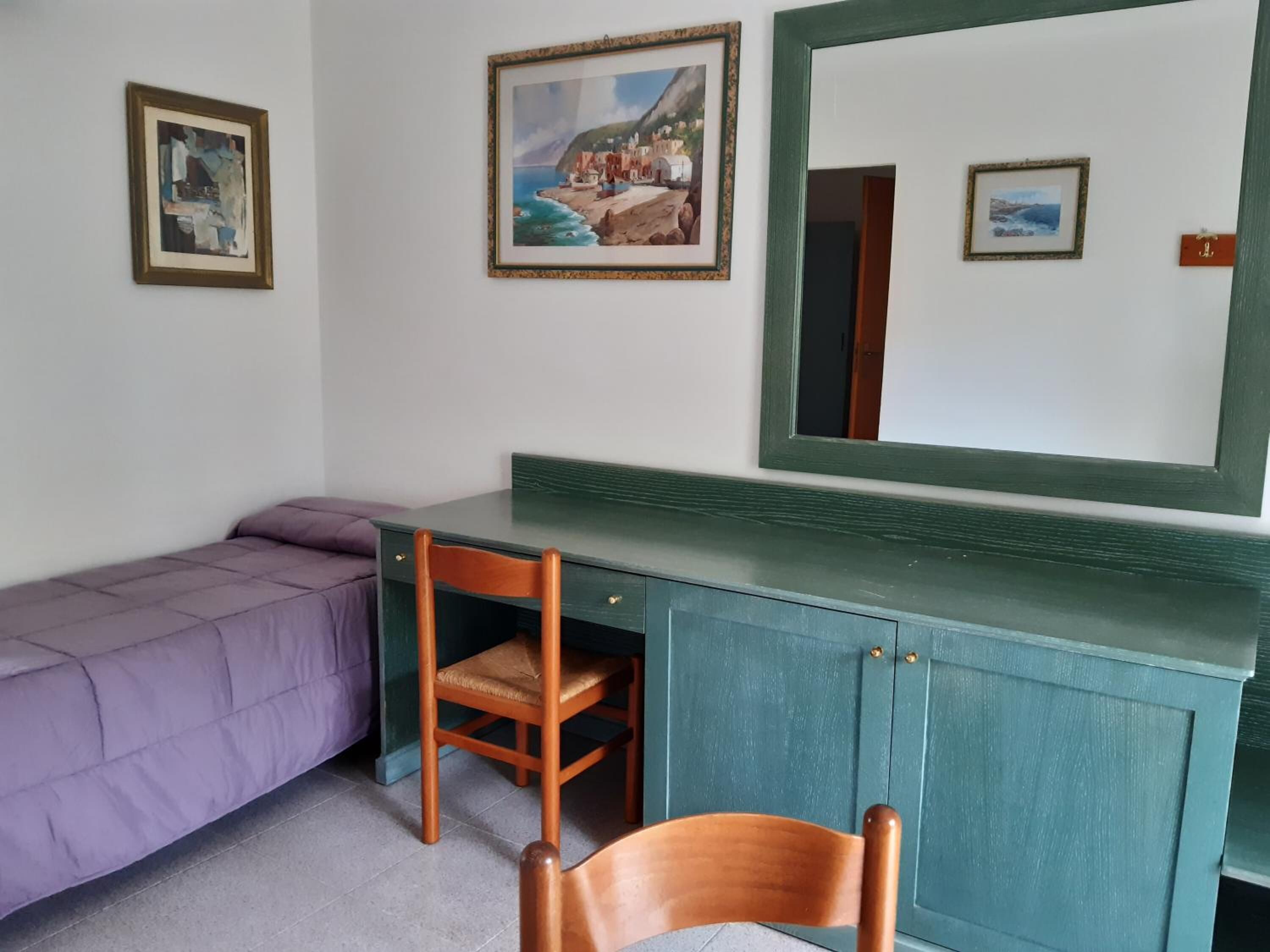 Una habitación con una cama, un escritorio y una silla. Hay dos cuadros en la pared.