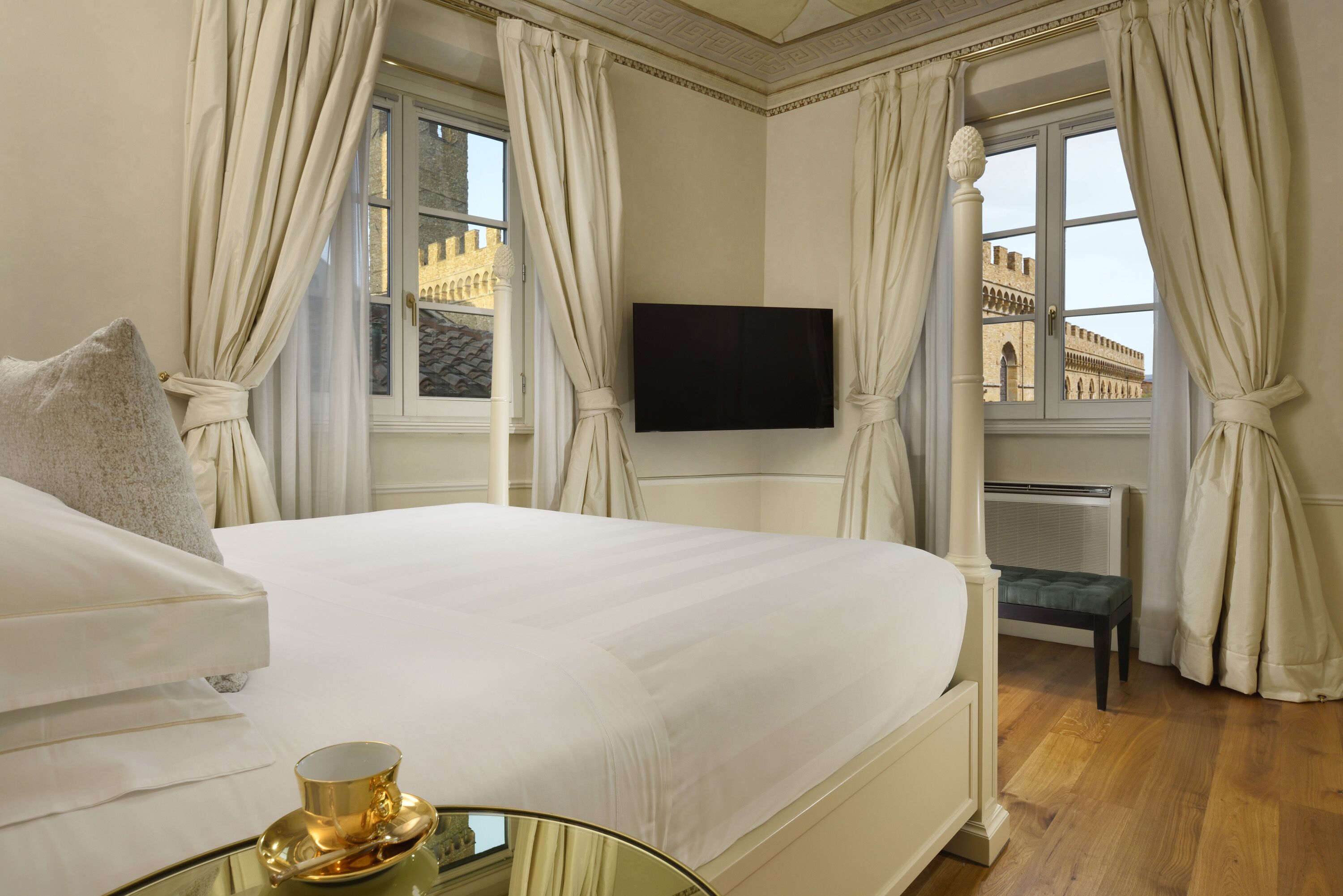 A hotel room with a large bed, a flat-screen TV mounted on the wall, and a view of a historic building through the window.