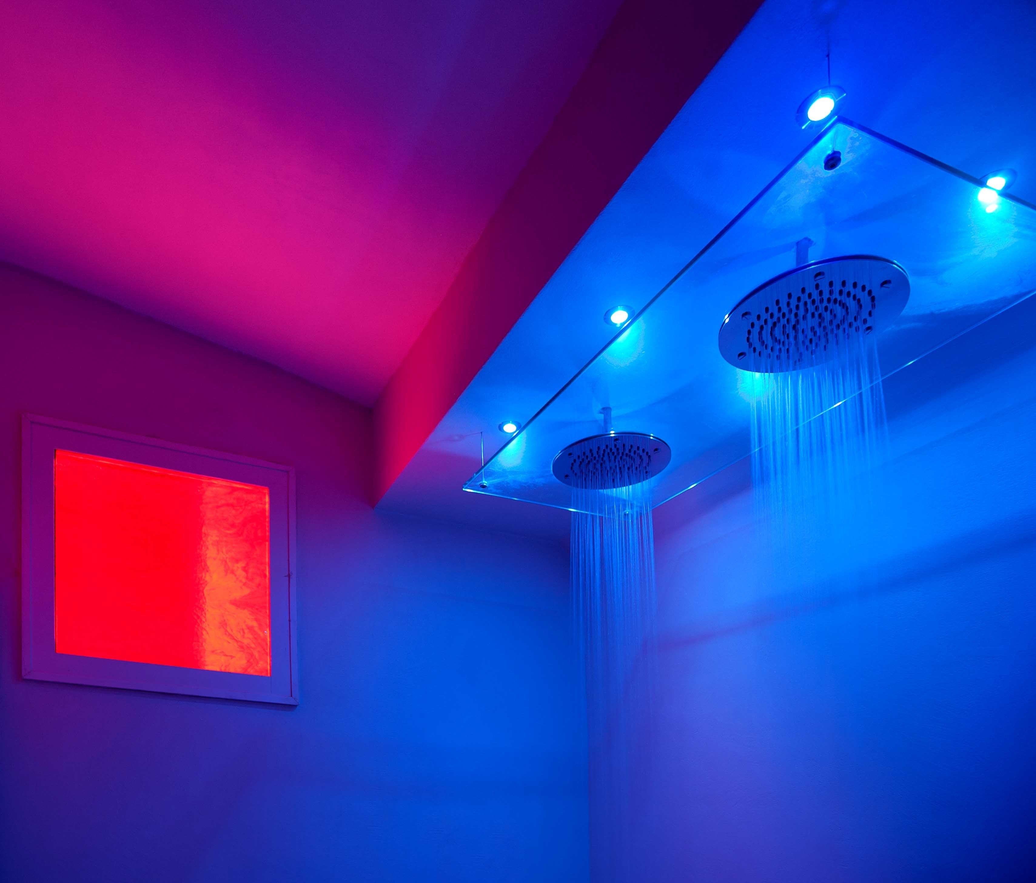 A modern bathroom with two showerheads and a red light panel on the wall.
