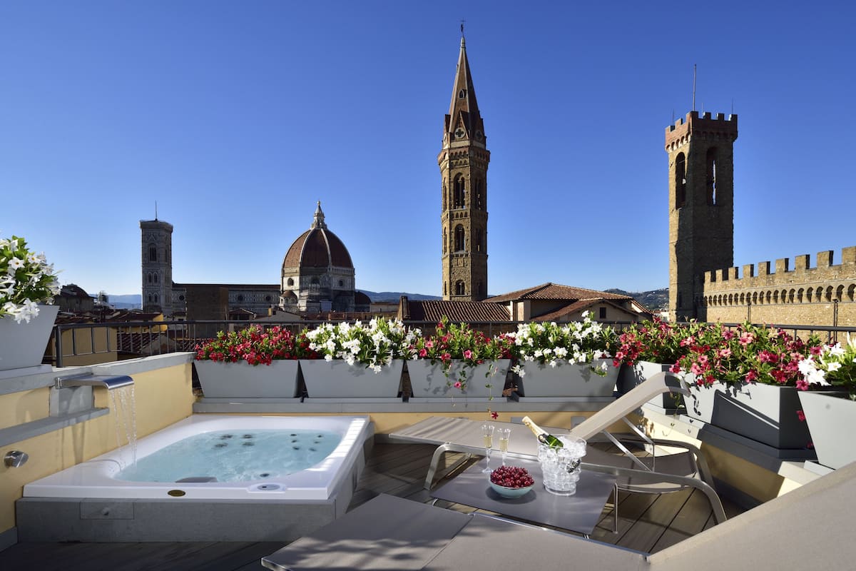A rooftop terrace with a hot tub, outdoor seating, and flower planters.