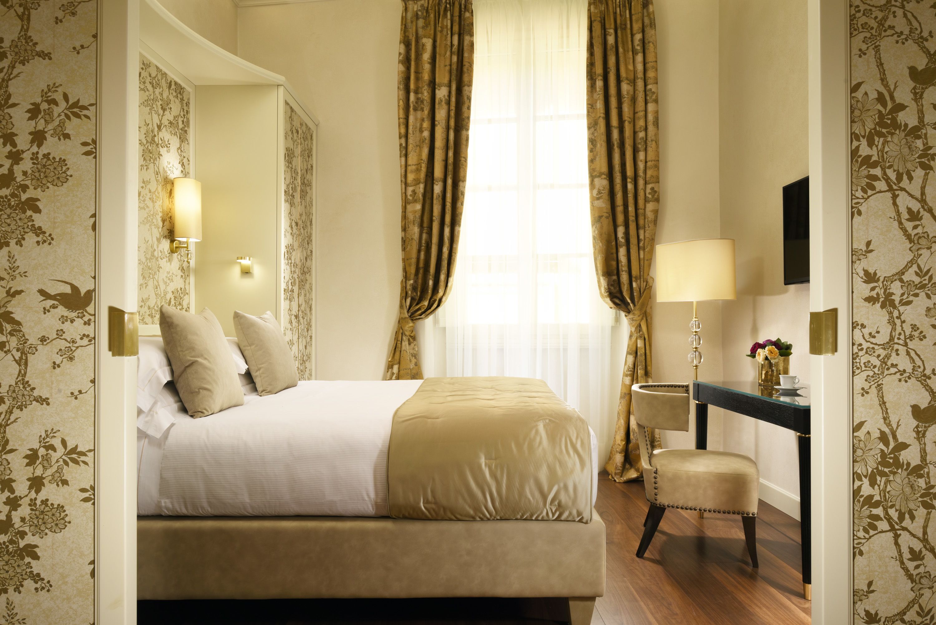 A hotel room with a bed, a desk, a chair, a lamp, and a large window with curtains.