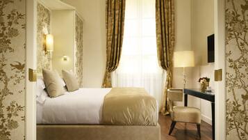 A hotel room with a bed, a desk, a chair, a lamp, and a large window with curtains.