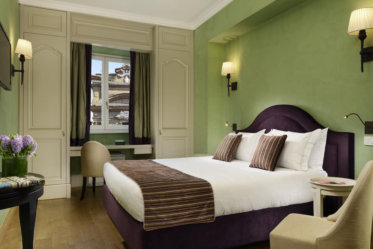 A neatly arranged bedroom with a large bed, a chair, a small table, and a window with curtains.