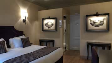A hotel room with a large bed, bedside tables, a desk, and framed artwork on the walls.