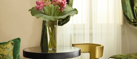 Una habitación con una mesa redonda de vidrio, una silla tapizada de verde y una silla amarilla con reposacabezas dorado.